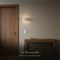 La Bienvenida: arbotante BURBIA WALL encendido en el recibidor junto a la puerta de nogal y la consola