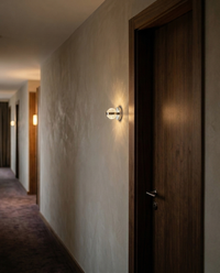Arbotante BURBIA WALL iluminando pasillo de hotel boutique junto al marco de puerta de nogal