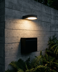Arbotante GIDI iluminando muro de concreto aparente sobre buzón negro en jardín de noche