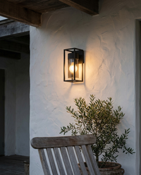 Lámpara de pared exterior VEGA II con luz cálida en terraza techada de muro blanco con olivo y silla de teca
